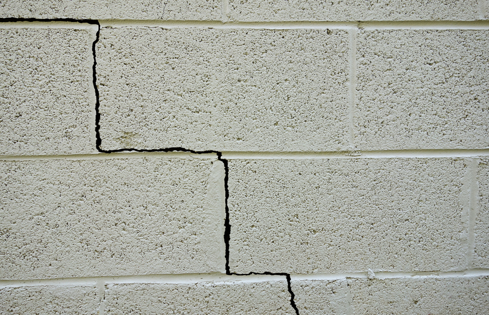 A concrete block wall with several visible cracks running through the blocks and mortar joints.